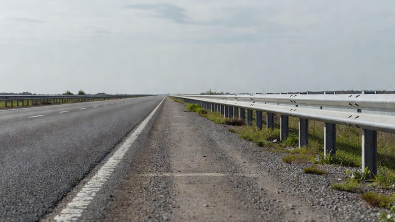 An empty road shoulder beside a crash barrier in flat daylight